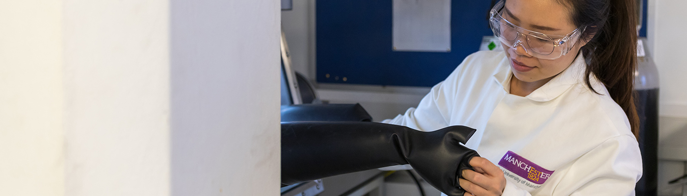 Female student in a lab coat pulling on rubber gloves