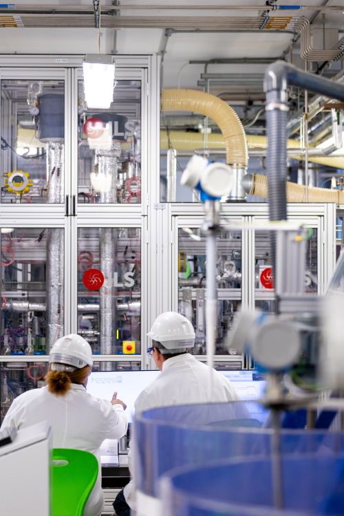 Two researchers reviewing control screens in a laboratory with enclosed process equipment.