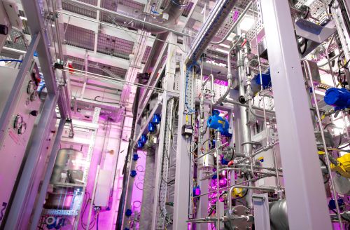 Industrial process rig with pipes, valves and sensors under coloured lighting.