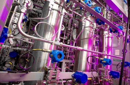 Close-up of stainless steel reactors and pipework with monitoring instruments in a pilot plant facility.