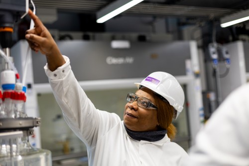 Researcher in safety helmet and goggles adjusting laboratory equipment in a process engineering facility.