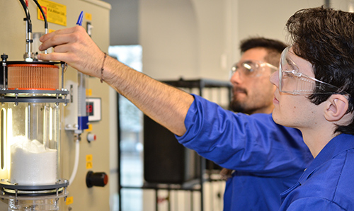 Two male researchers in lab coats stretching across to operate specialist equipment