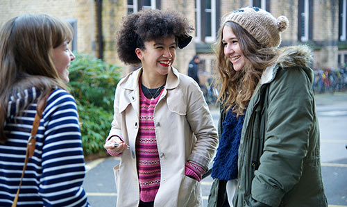Three female students smiling while in discussion on campus